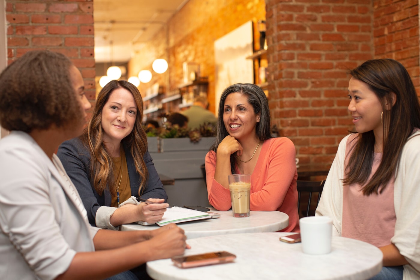 Four women sitting together around a café table, listening to one another.